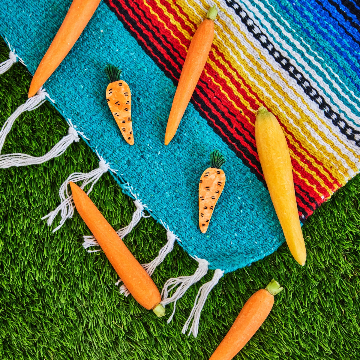 Carrots and a yellow squash on a colorful woven mat with grass background