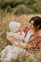 Woman holding a baby in a field of tall grass and wildflowers