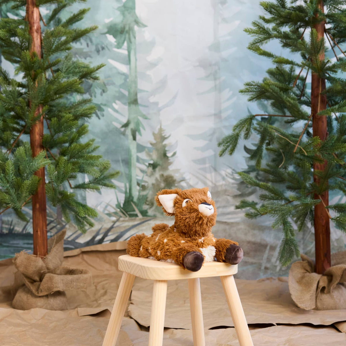 Plush deer toy on a wooden stool with a forest background