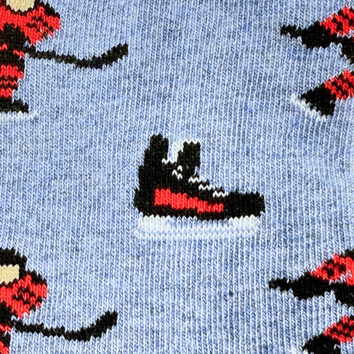 Close-up of a knit fabric with a light blue background and a repeating pattern of hockey players and ice skates in black, red, and white.