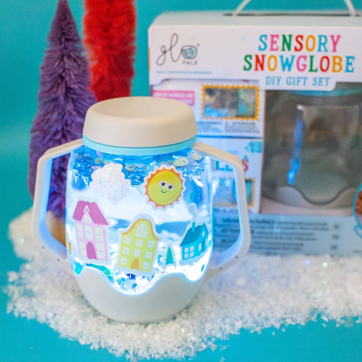 Sensory snowglobe with colorful houses and sun, next to a DIY gift set packaging on a blue background.