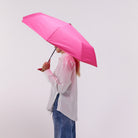 Person holding a pink umbrella against a plain background