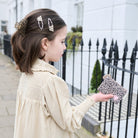 Woman with leopard print hair clips and clutch in front of a black iron gate.