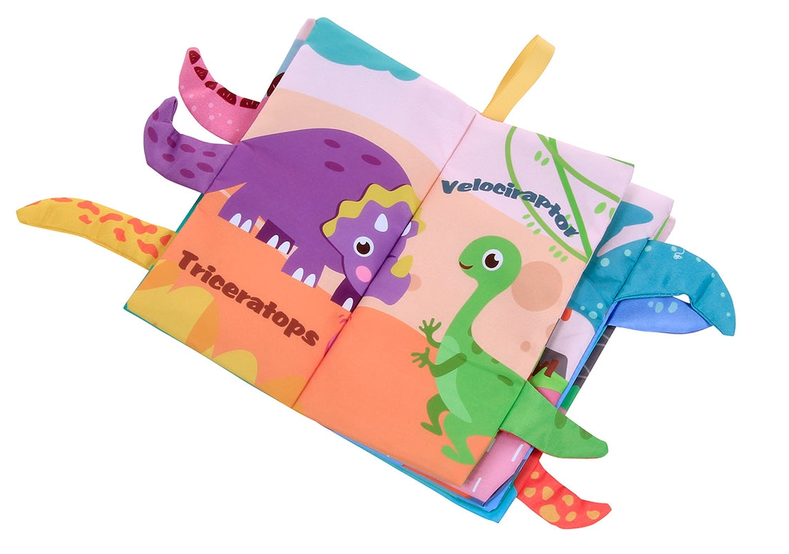 A colorful fabric baby book with dinosaur-themed pages and soft toy dinosaur wings attached along the sides, photographed on a plain white background.