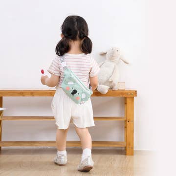 Child holding a plush toy and a small bag in a minimalistic room.