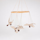A fabric bird mobile hanging from a light wood ring with four cream-colored plush birds with dark brown beaks and legs, suspended against a plain white background.