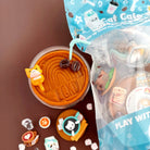 Cup of coffee with a bear-shaped stirrer, surrounded by small decorative items on a brown surface.