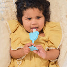 Child in a yellow outfit holding a blue teething toy with a white object inside.
