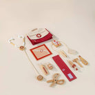 A wooden toy doctor kit with a red and cream fabric bag, stethoscope, blood pressure monitor, scissors, syringe, medicine bottles, and other medical accessories arranged on a white background.