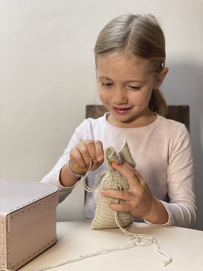 Young girl holding a small woven bag at a table with a plain background