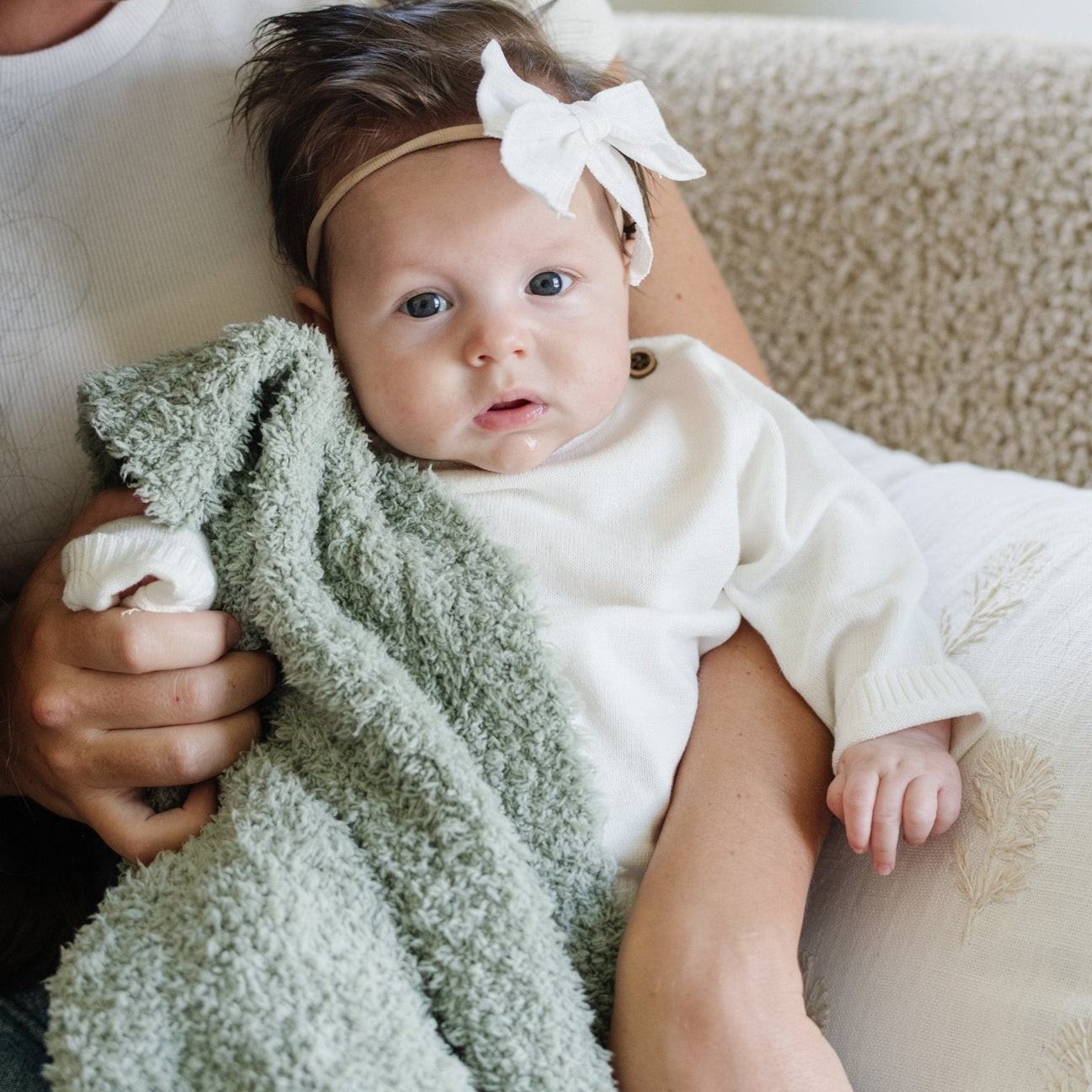Baby wrapped in a green blanket with a white headband, lying on a beige surface.