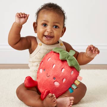 Baby holding a strawberry-shaped toy with a plain background