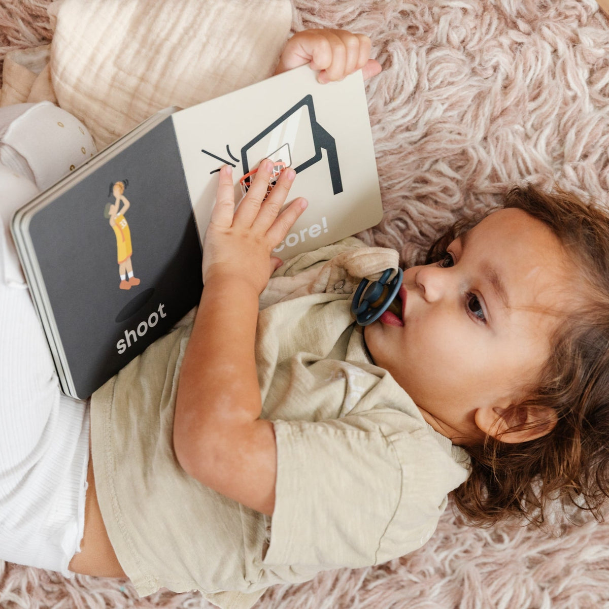 Child lying on a fluffy pink rug reading a book titled 'shoot'.