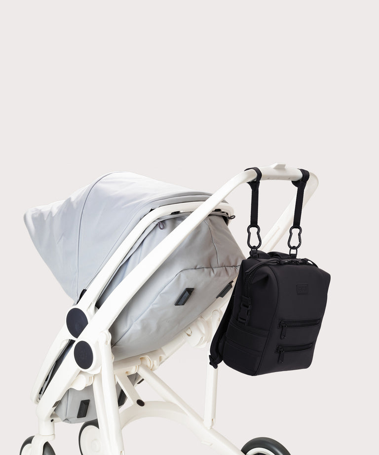 Black backpack attached to a white stroller on a light gray background