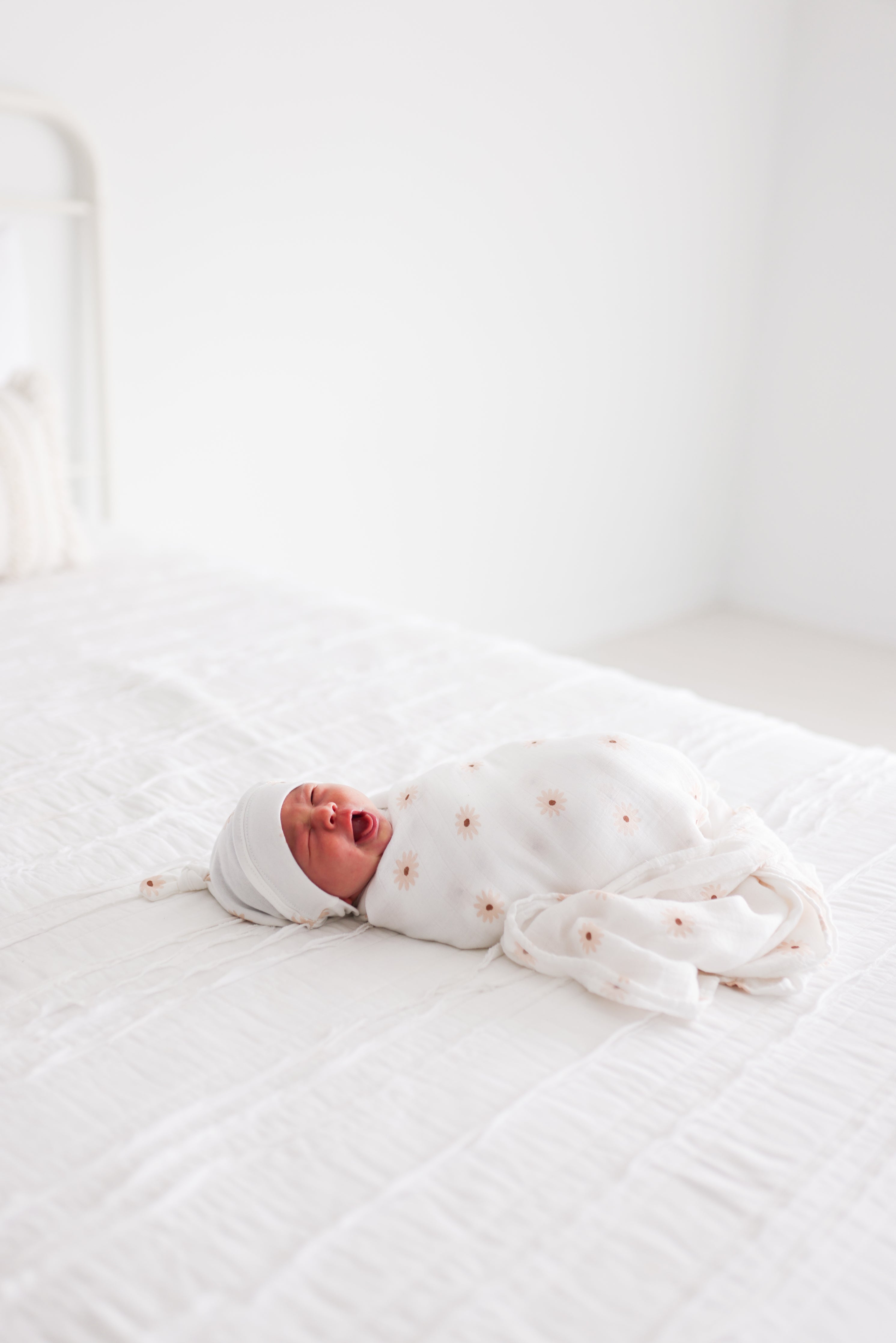 alt text for this image
A newborn baby swaddled in a white blanket with a delicate daisy pattern, sleeping peacefully on a white bed.