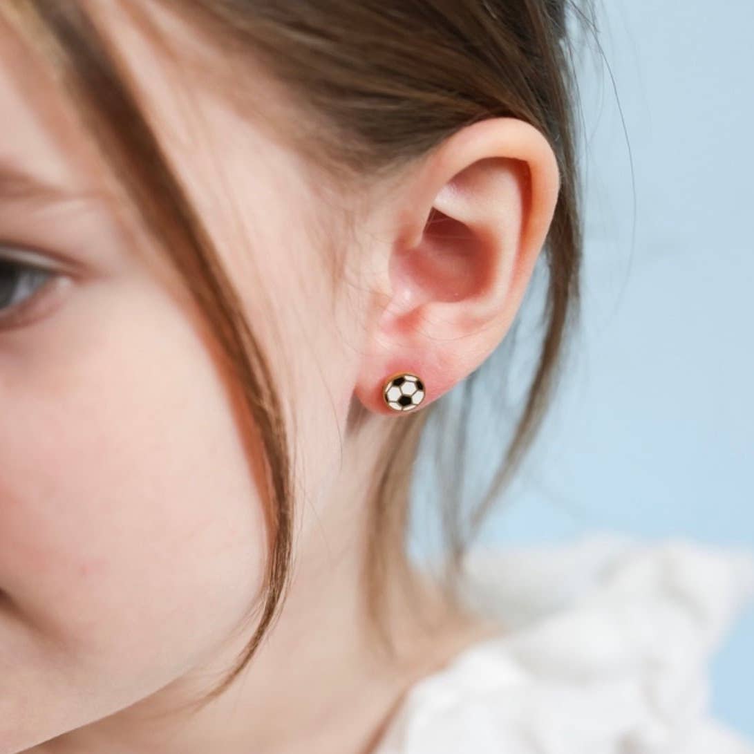 Close-up of a person wearing a gold soccer ball earring with a blurred background