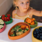 Colorful toy vegetables on a table with a child in the background