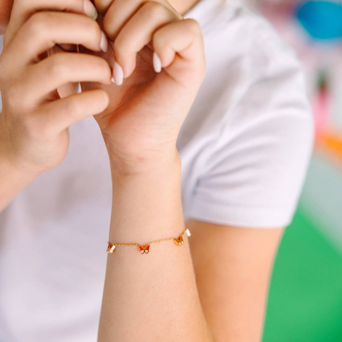 Close-up of a hand wearing a gold bracelet with small beads against a blurred background