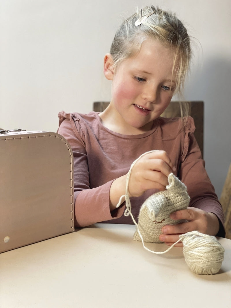 Young girl knitting with yarn and a knitting needle on a table.