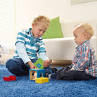 Two children playing with blocks on a blue carpet in a living room.