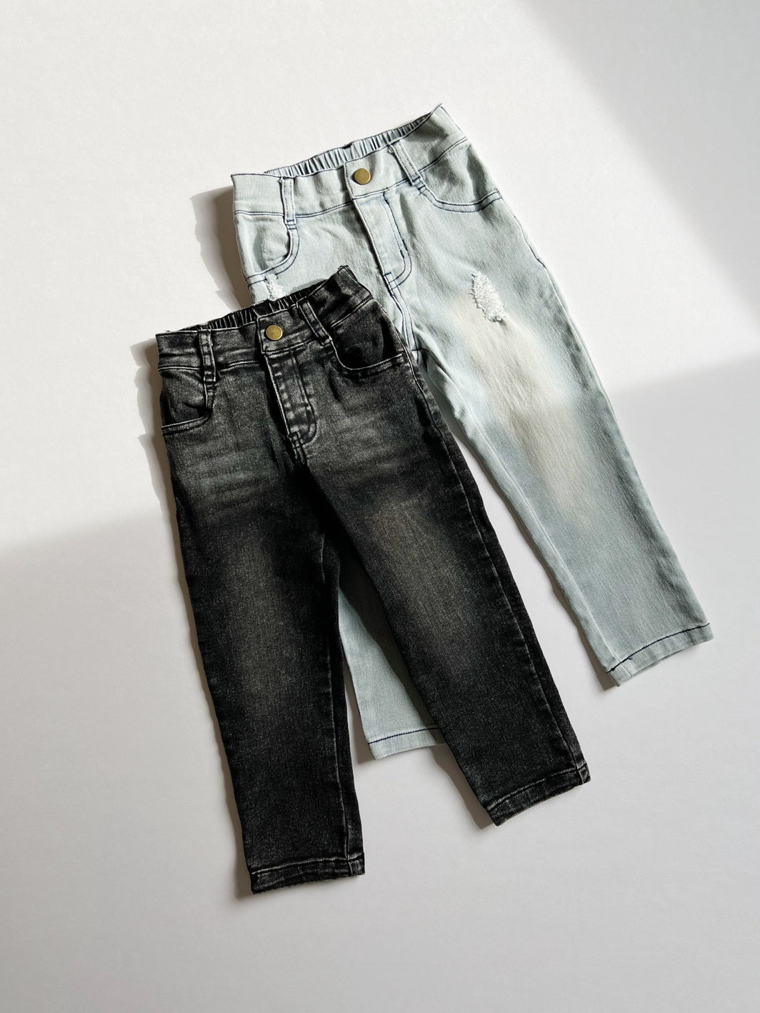 Two pairs of jeans, one black and one light blue, on a white background