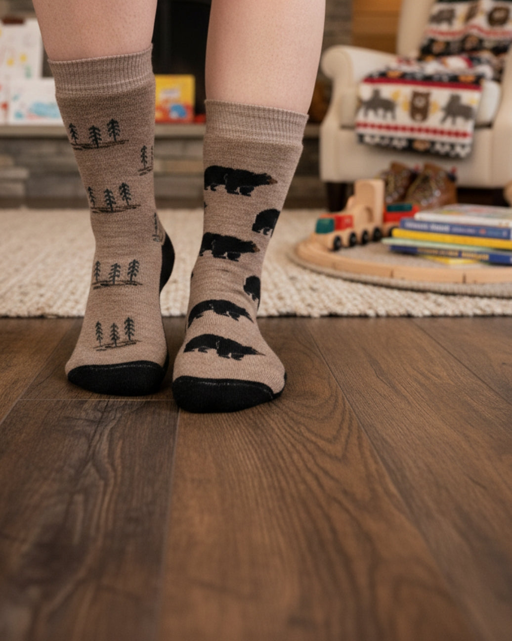 A person's feet wearing beige crew socks with black printed polar bear and tree patterns, standing on a dark wood floor in a cozy room setting.