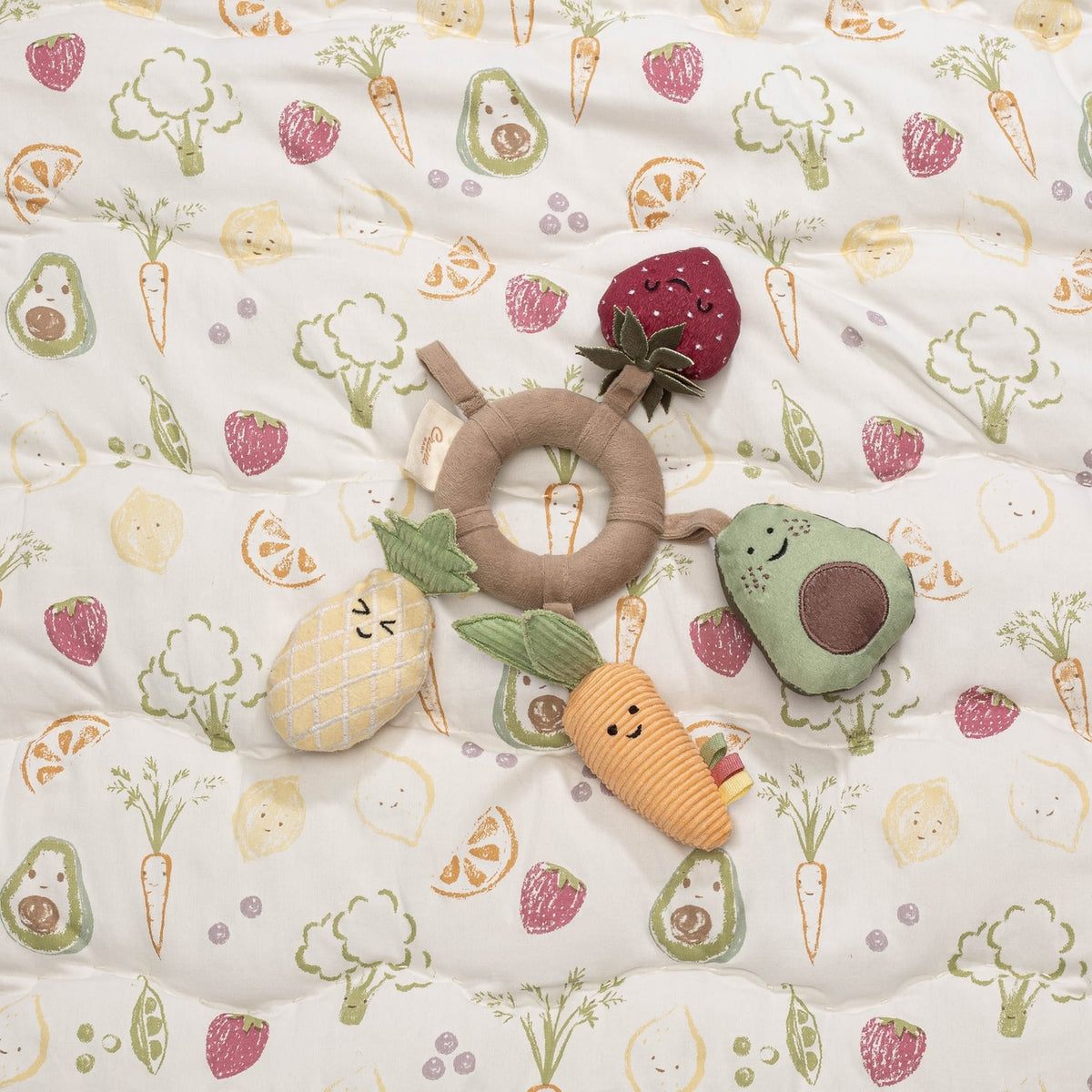 Set of baby toys on a crib sheet with fruit and vegetable pattern