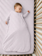 A baby sleeping in a günamüna Sleep Sack in a charming pink-and-white gingham pattern featuring a convenient diagonal zipper