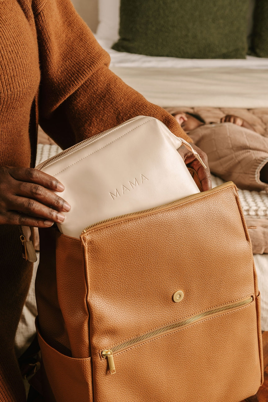 Person holding a white pouch with 'MAMA' printed on it, placed inside a brown leather bag.