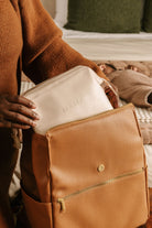 Person holding a white pouch with 'MAMA' printed on it, placed inside a brown leather bag.
