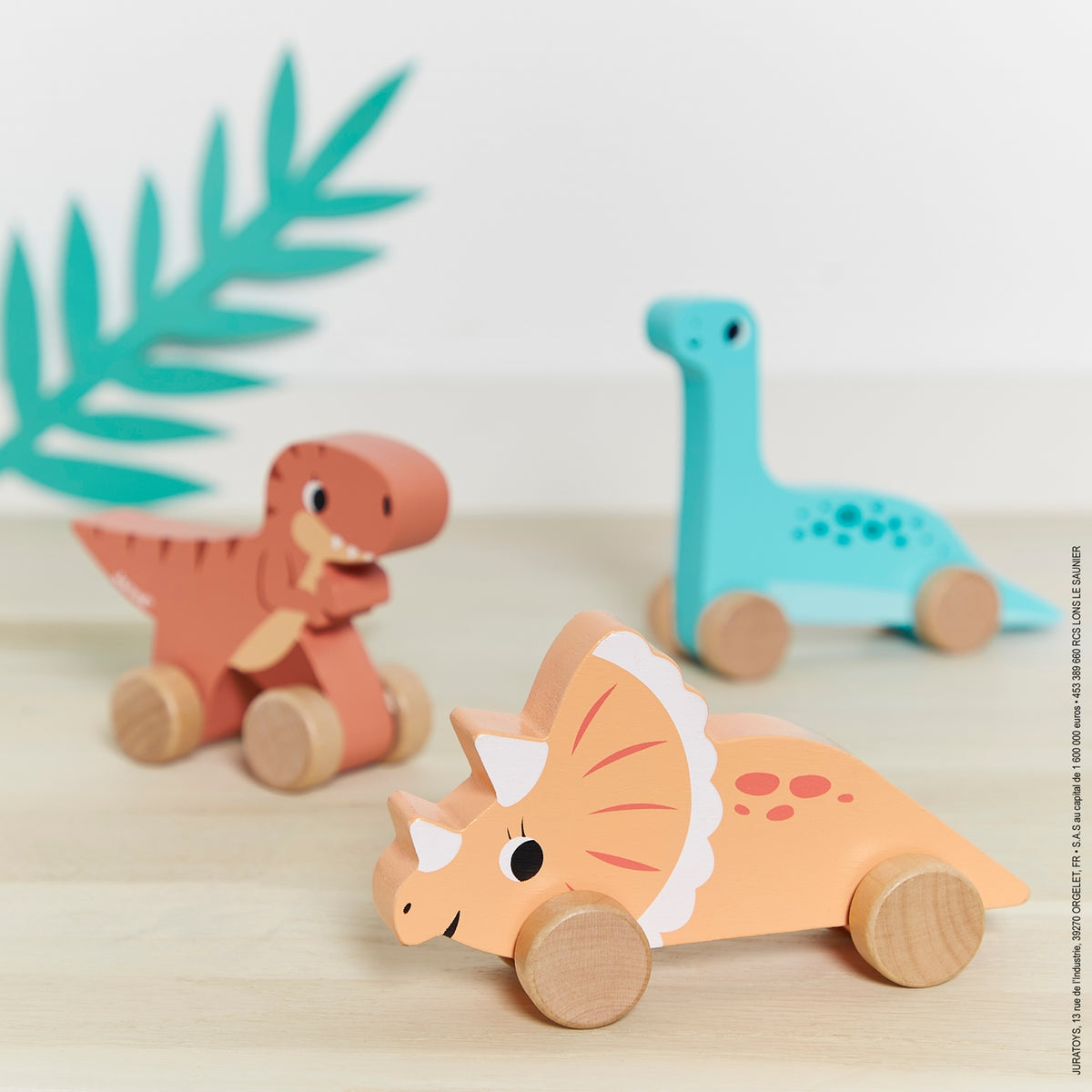 Three wooden dinosaur toys on a light surface with a decorative leaf.