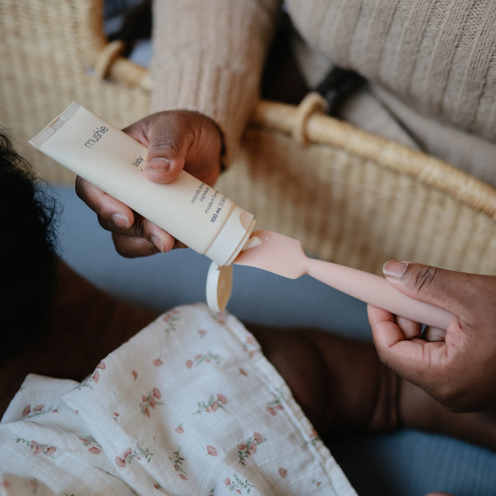Person applying lotion to a child's hand with a focus on the product and action.