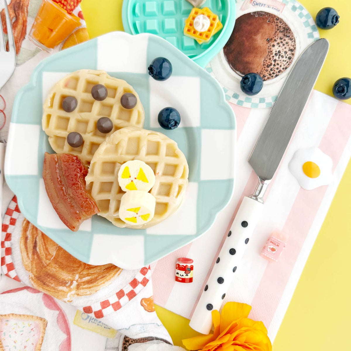 Waffles with berries on a checkered plate with a knife and decorative items.