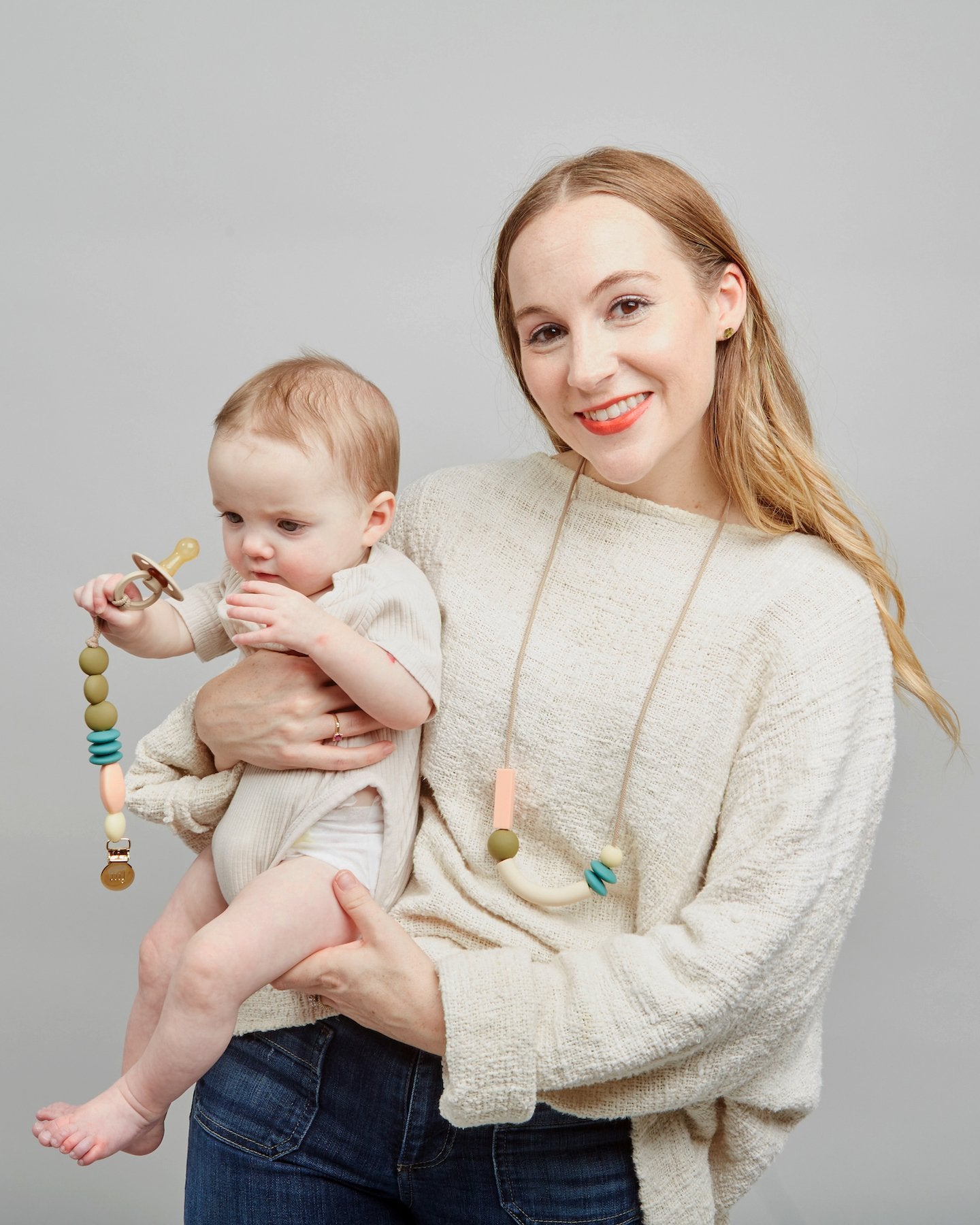Woman holding a baby with a teething toy against a gray background
