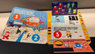 A close-up of a children's hockey-themed board game showing illustrated instruction cards and a scoring card on a dark tabletop.