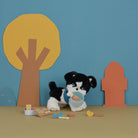 Toy dog with a bowl and treats in front of a blue wall with tree and house shapes.