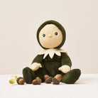 Stuffed toy dressed in green with a hood, sitting on a white surface with acorns.