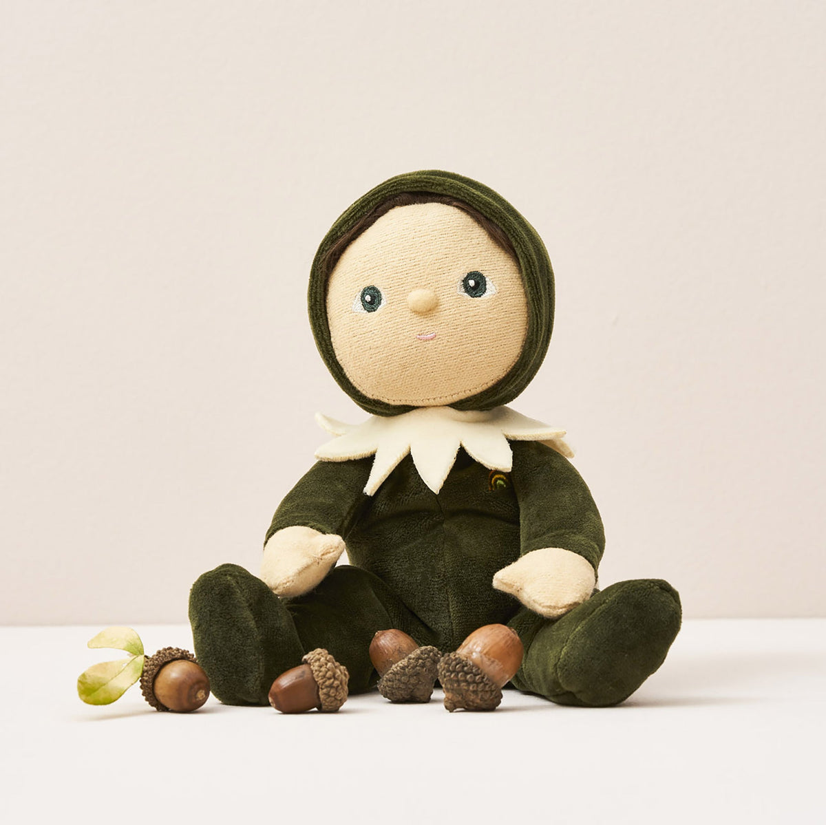 Stuffed toy dressed in green with a hood, sitting on a white surface with acorns.