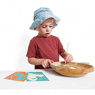 Child playing with a wooden bowl and spoon on a white surface