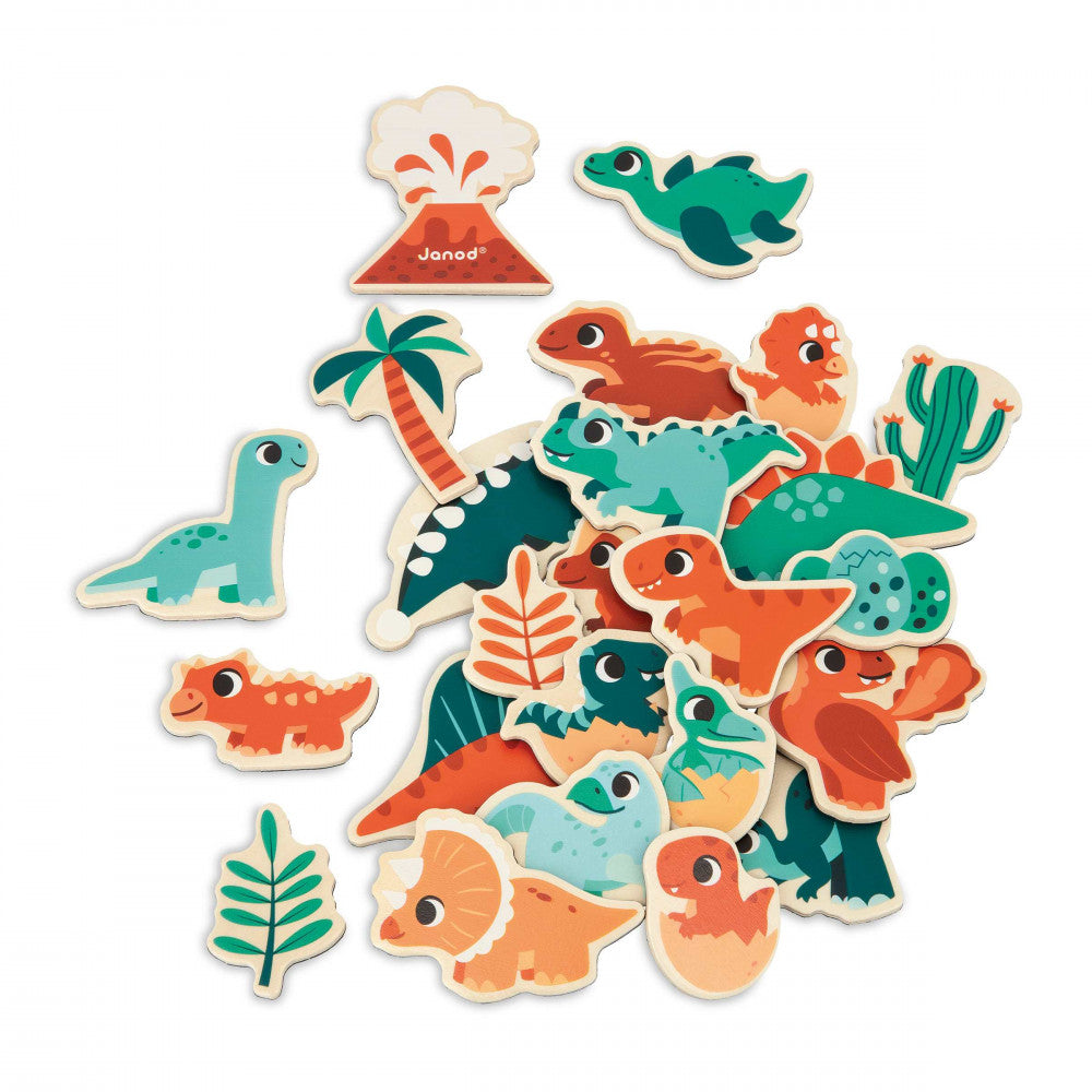 A pile of colorful wooden dinosaur and prehistoric-themed puzzle pieces on a white background, including various dinosaurs, a volcano, palm tree, cactus, and leaves. The brand name 'Janod' is visible on one piece.