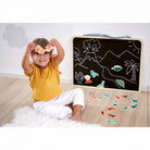 Child playing with stickers and a blackboard with drawings on a wooden floor.