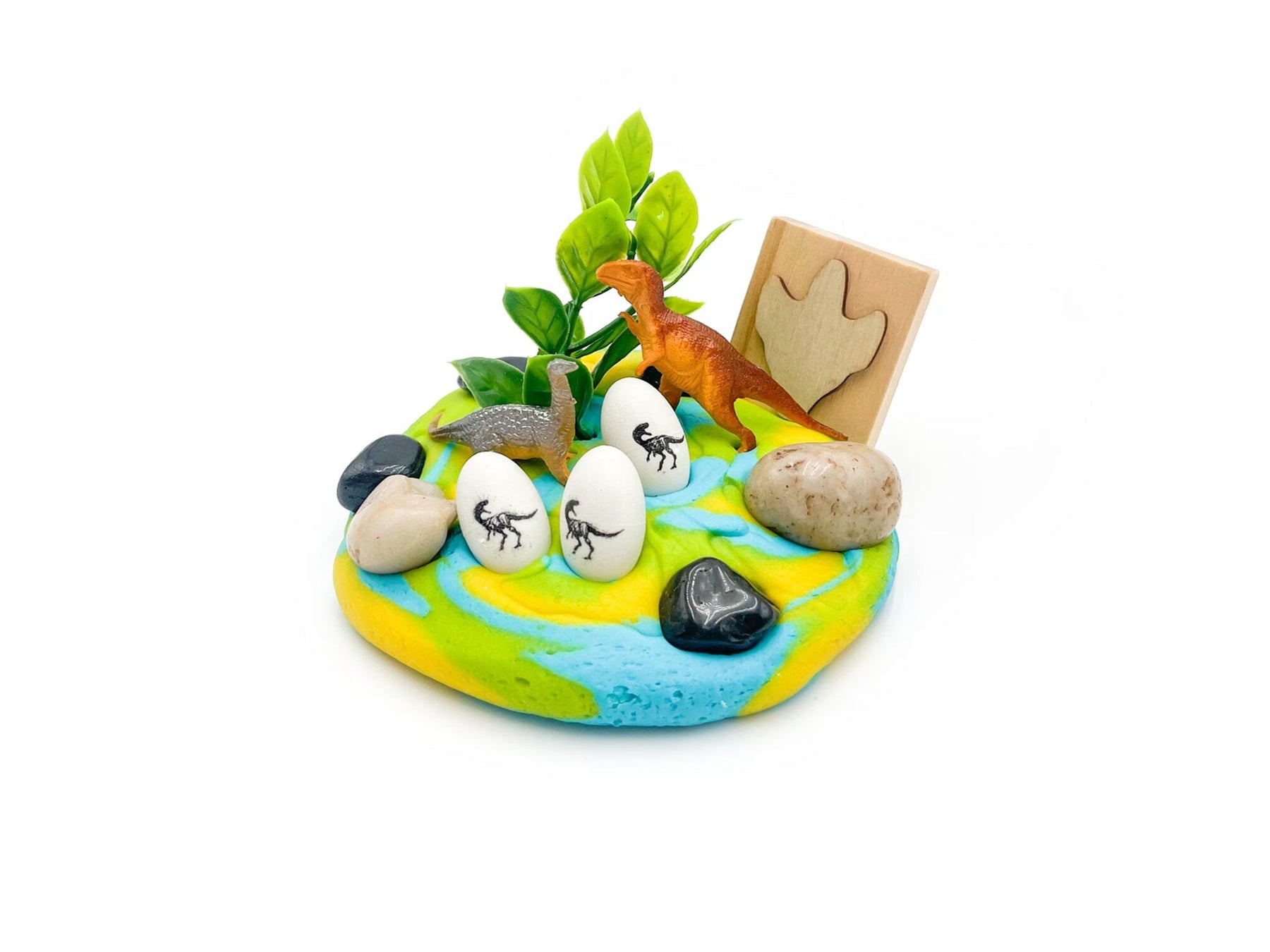 Miniature diorama with dinosaur figures, eggs, and plants on a white background