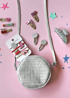 Small round silver bag with hair clips on a pink background
