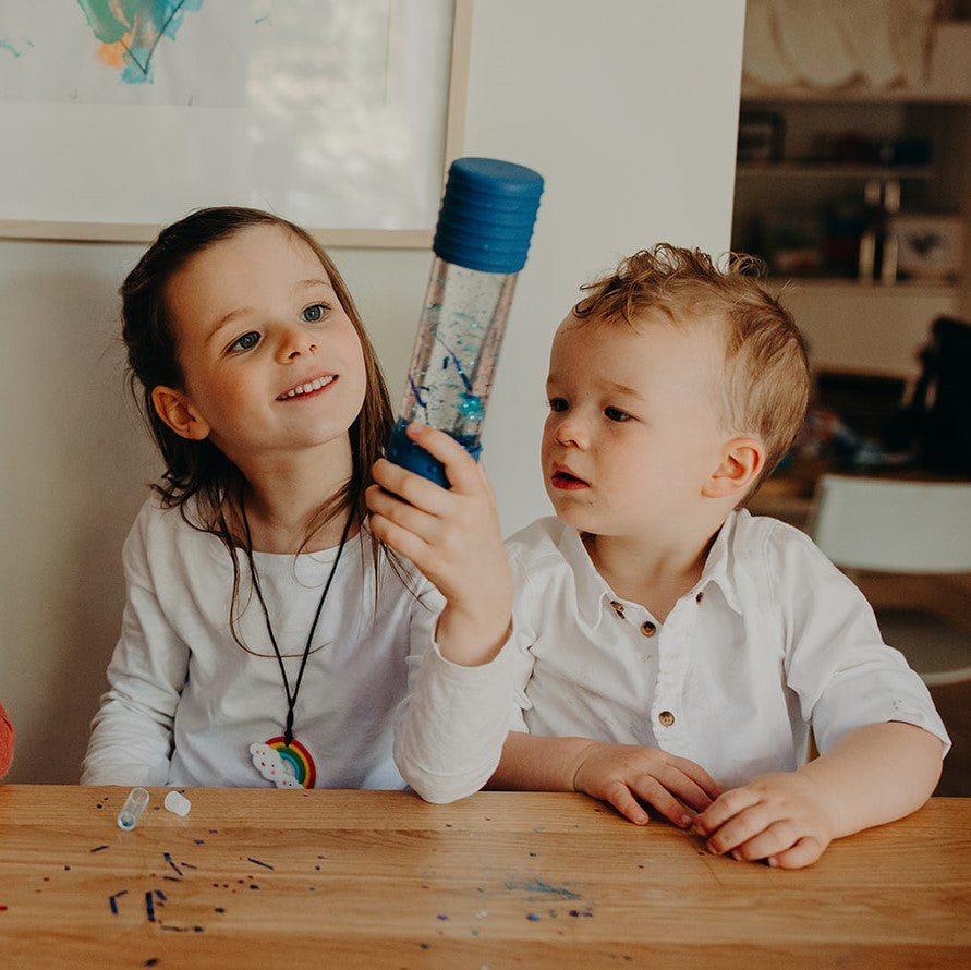 Two children sitting at a table with a water bottle, in a casual indoor setting.
