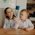 Two children sitting at a table with a water bottle, in a casual indoor setting.