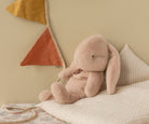 Pink plush bunny toy on a bed with decorative pillows and a flag in the background.