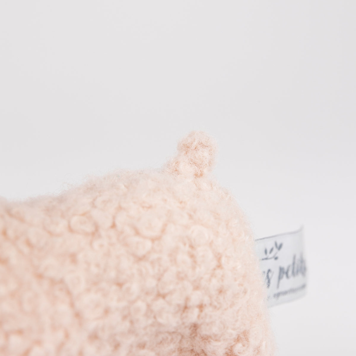 Close-up of a soft, textured plush lamb tail in a cream color, showing a small fabric tag.