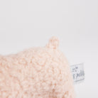 Close-up of a soft, textured plush lamb tail in a cream color, showing a small fabric tag.