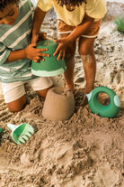 Two children playing with sand toys on a sandy surface
