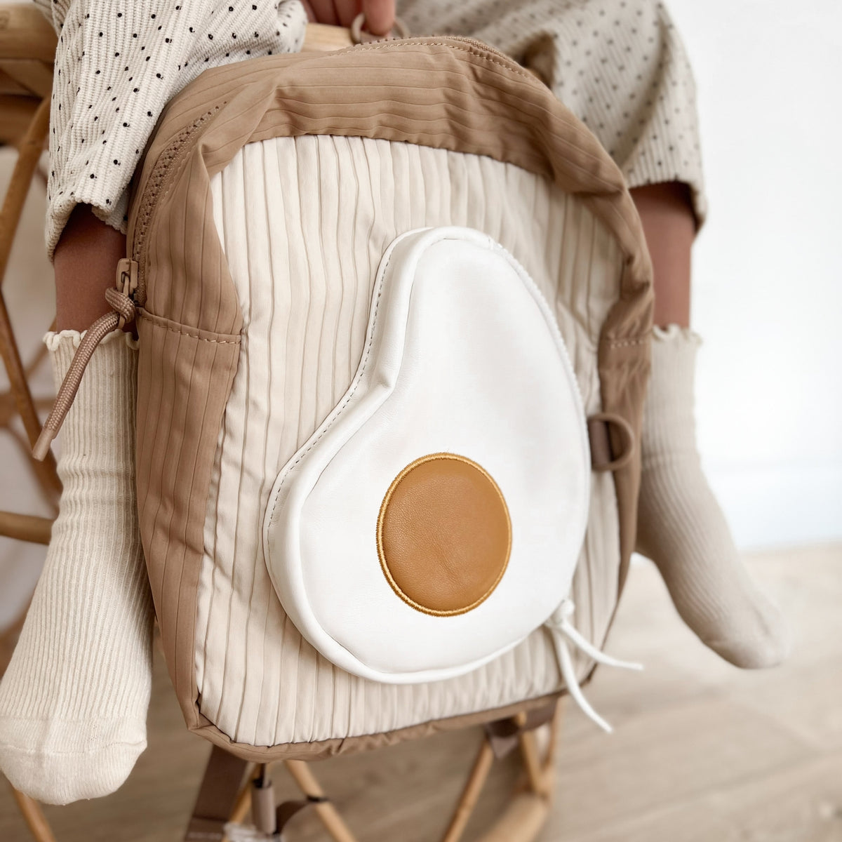 Close-up of a baby carrier with a white cushion and brown accents, worn by a person.